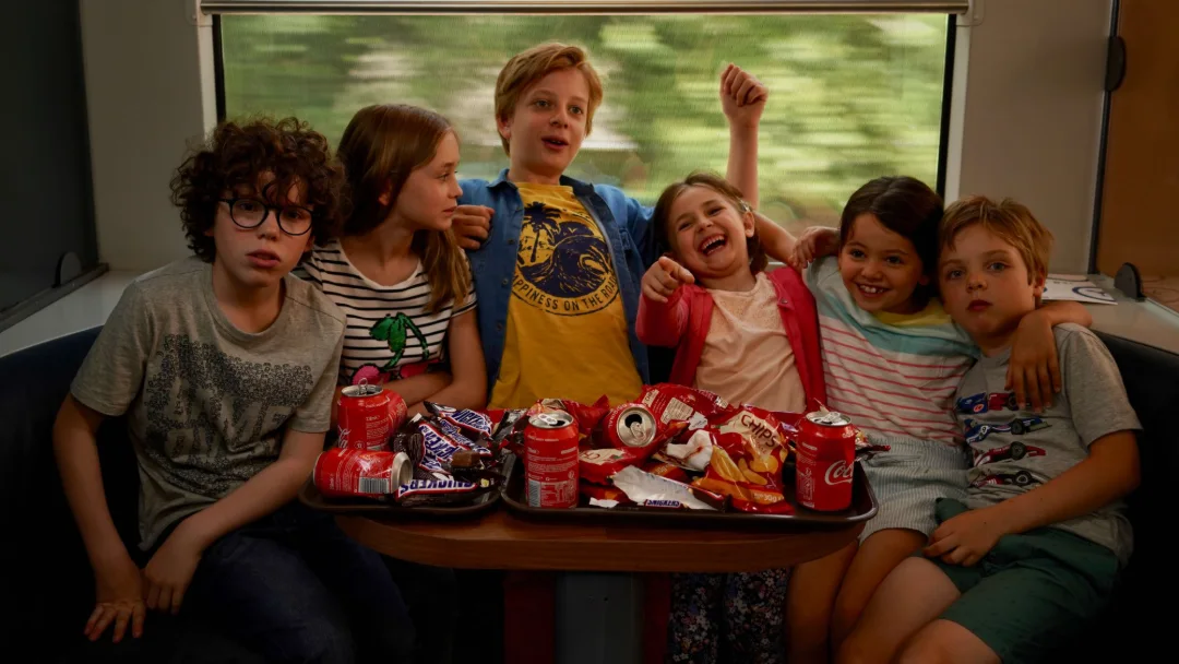 Six enfants entassés sur une banquette de train, des friandises sur la tablette.