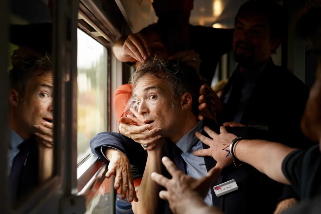 Un homme coincé à la fenêtre d'un train, entouré de mains.
